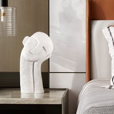 a white sculpture sitting on top of a bed next to a night stand and lamp