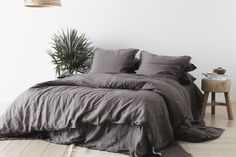 the bed is made up with grey linens and pillows, along with a potted plant