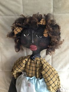 a black doll with curly hair wearing a yellow and blue dress on top of a white sheet