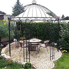 an outdoor dining area with a gazebo and table in the middle, surrounded by greenery