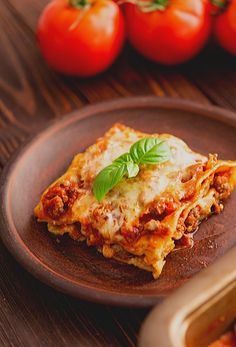 a brown plate topped with lasagna covered in cheese and sauce next to tomatoes