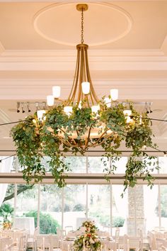 a chandelier hanging from the ceiling with greenery and candles on it at a wedding reception