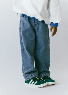 a small child wearing blue jeans and a white shirt is standing with his hands in his pockets