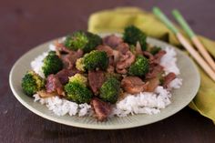 a plate with rice, broccoli and meat on it next to chopsticks