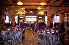 a room filled with lots of tables covered in purple and silver table cloths next to tall chandeliers