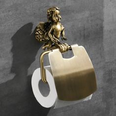 a gold toilet paper holder with a little angel on it's side and a roll of toilet paper in the other hand