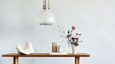 a wooden table topped with vases filled with flowers next to a white light fixture