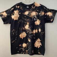 a black shirt with gold paint splattered all over it and a white tag on the chest