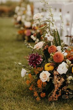 a bunch of flowers that are sitting in the grass next to some chairs on the ground