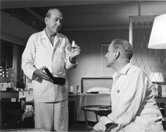 an old photo of a man in a hospital room talking to another man who is sitting down