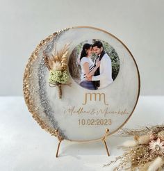 a white and gold wedding photo frame with a couple on it next to dried flowers