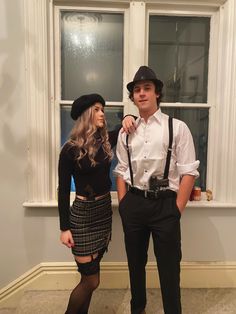 a man and woman dressed up in costume posing for a photo by a window with their hats on