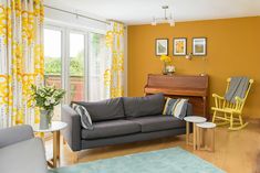 a living room filled with furniture and a piano in front of a yellow curtained window