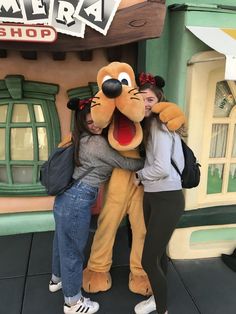 two girls hugging pluto the dog in front of mickey mouse's shop at disney world