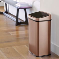 a brown trash can sitting on top of a wooden floor next to a white couch