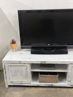 an old white tv stand with a basket on top and a potted plant next to it