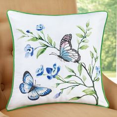 a white pillow with blue and green butterflies on it sitting on a chair in front of a window