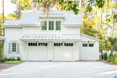 a white house with two garages in front of it and trees around the yard