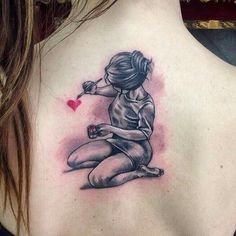 a woman with a tattoo on her back holding a red heart and sitting on the ground