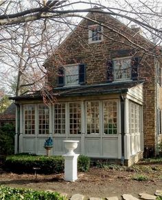 an old brick house with white trim on the front and side windows, surrounded by shrubbery