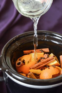 an orange being poured into a crock pot filled with cinnamons and apple slices