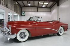 an old red and white car parked in a garage next to a clock on the wall