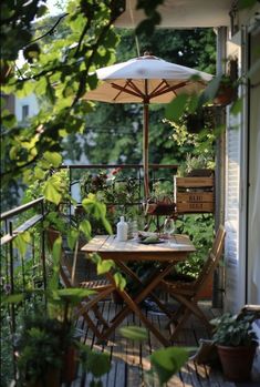 an outdoor table and chairs on a wooden deck with umbrella over it, surrounded by potted plants