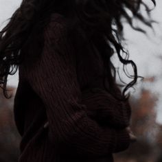 a woman with long hair standing in front of trees