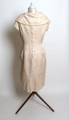 "Very pretty dress made of creamy heavy taffeta satin fabric with a tinge of pink. The fabric has a floral design. Grand shawl collar and a bow under the bust. The dress has a metal zipper up the back and is carefully concealed with a flap so it remains invisible. The zipper ends just below the collar. In excellent condition. Measurements are approximate: Bust - 38\", Waist - 29\", Hips - 45\". Modern-sized 10." Elegant Cream Vintage Dress With Fitted Bodice, Elegant Vintage Cream Dress With Fitted Bodice, Elegant Vintage Dress With Fitted Bodice, Elegant Lined Dress For Vintage Fashion, Silk Cream Dress For Vintage Events, Cream Silk Dress For Vintage Events, Elegant Lined Vintage Wedding Dress, Elegant Lined Vintage Dress, Elegant Cream Dresses For Vintage Fashion