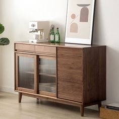 a wooden cabinet sitting next to a potted plant and a framed print on the wall