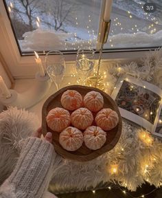 a wooden bowl filled with oranges on top of a table next to a window