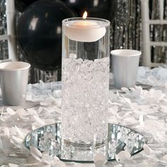 a candle that is inside of a glass vase on a table with confetti