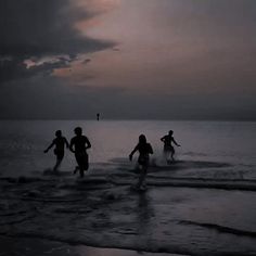 three people running into the ocean at night with dark clouds in the sky behind them