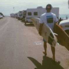 a man holding a surfboard while standing on the side of a road next to parked cars