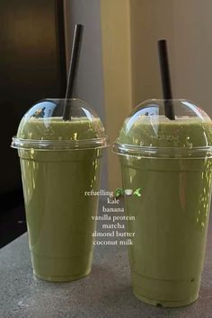 two green smoothies with straws in them sitting on a counter next to each other