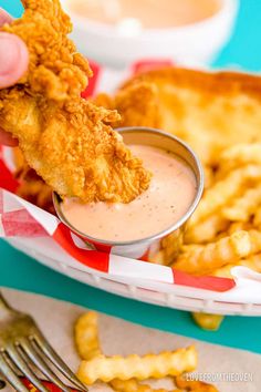 a person dipping something into a small bowl filled with sauce on top of fried food