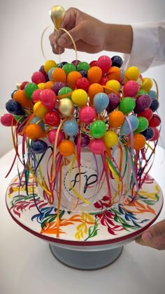 a cake decorated with colorful candies on top of a white table and someone holding a balloon above it