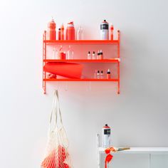 an orange shelf with bottles and bags hanging from it's sides next to a white wall