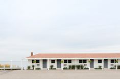 a white building with black shutters next to a parking lot and ocean in the background