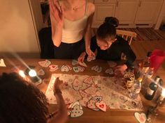 two women sitting at a table with decorated cookies on it and candles in front of them