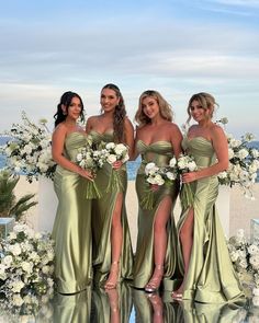 four bridesmaids pose for a photo in front of an outdoor ceremony arch with white flowers and greenery