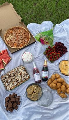 an assortment of food is laid out on a blanket in the grass, including pizza and watermelon