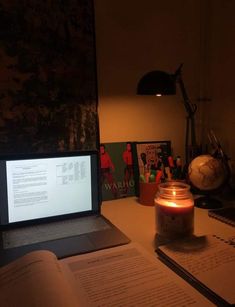 an open book sitting on top of a desk next to a laptop computer and a lit candle