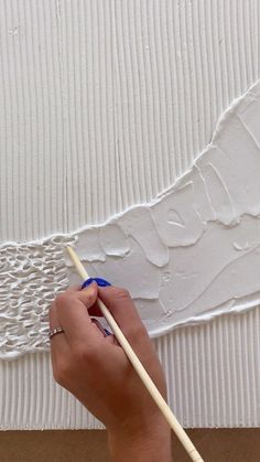 a person is painting a wall with white paint and a blue brush in their hand