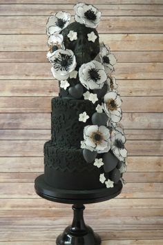 a black wedding cake with white flowers on the top and bottom, sitting on a wooden table