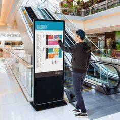 a man standing next to an escalator pointing at a poster on the wall