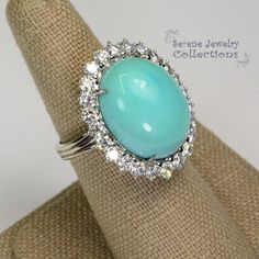 This unique light greenish blue turqoise is special in that it has not been stabilized but has kept color over the years. Brilliant round diamonds encircle the turquoise.Ring Size: 6.5Total Weight: 19.88 gramsPrecious Metal: 18k goldPrecious stones:-Sleeping Beauty Turquoise Center Stone: 18.1mm x 14.5mm-White Round Diamonds: 2 carats Formal Turquoise Oval Rings, Turquoise Ring With Halo Setting In Fine Jewelry Style, Fine Jewelry Turquoise Ring With Halo Setting, Turquoise Halo Setting Fine Jewelry Ring, Elegant Oval Turquoise Ring With Center Stone, Heirloom Turquoise Gemstone Ring For Formal Occasions, Oval Diamond Turquoise Ring For Formal Occasions, Formal Oval Turquoise Ring With Diamond, Heirloom Style Turquoise Ring For Formal Occasions