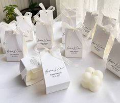 small white boxes with tags on them sitting on a table next to candles and flowers