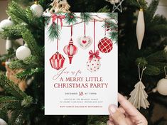 a person holding up a christmas party card in front of a tree with ornaments on it