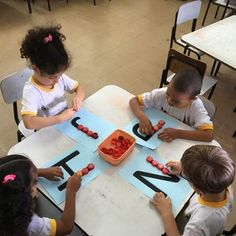 three children sitting at a table making letters with strawberries